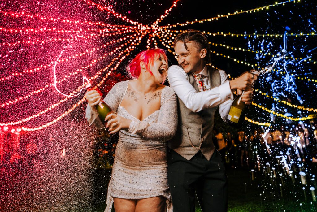 Bride and groom spraying champagne together during twilight wedding photos in the UK
