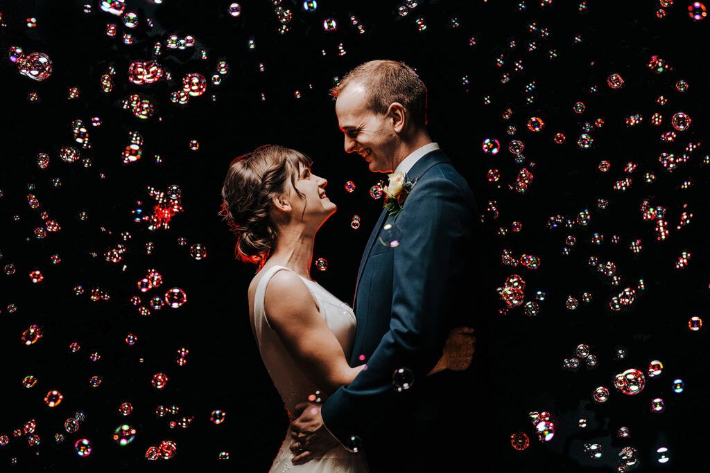 Bride and groom surrounded by bubbles during evening wedding portraits in Surrey, creative image by Alex Buckland Photography