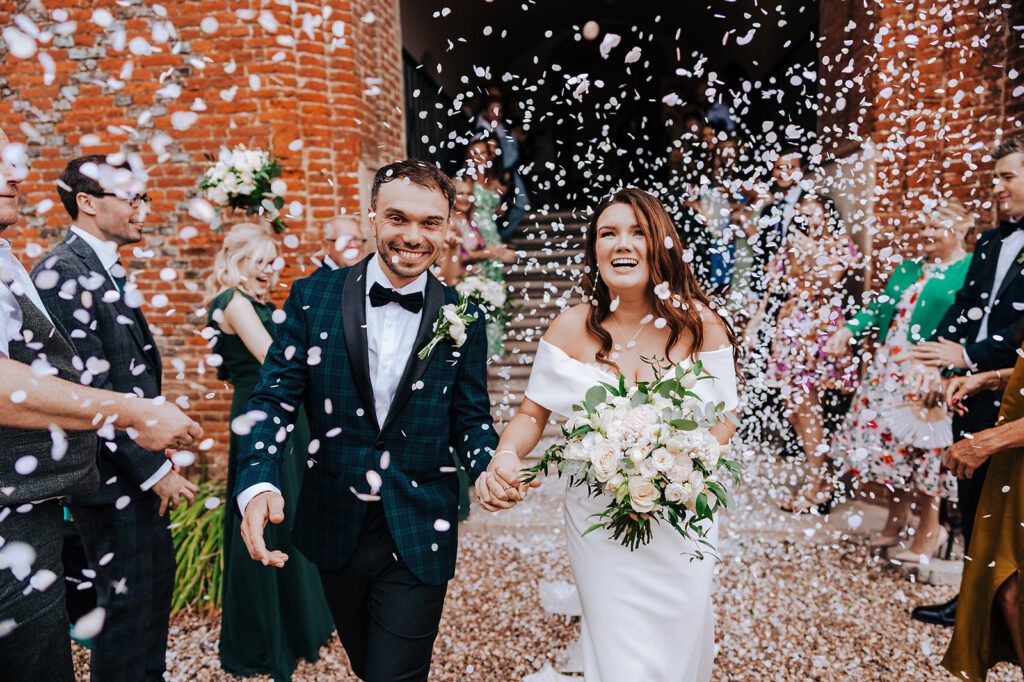 Bride and groom laughing during confetti throw outside a church in Kent, documentary wedding photo by Alex Buckland Photography