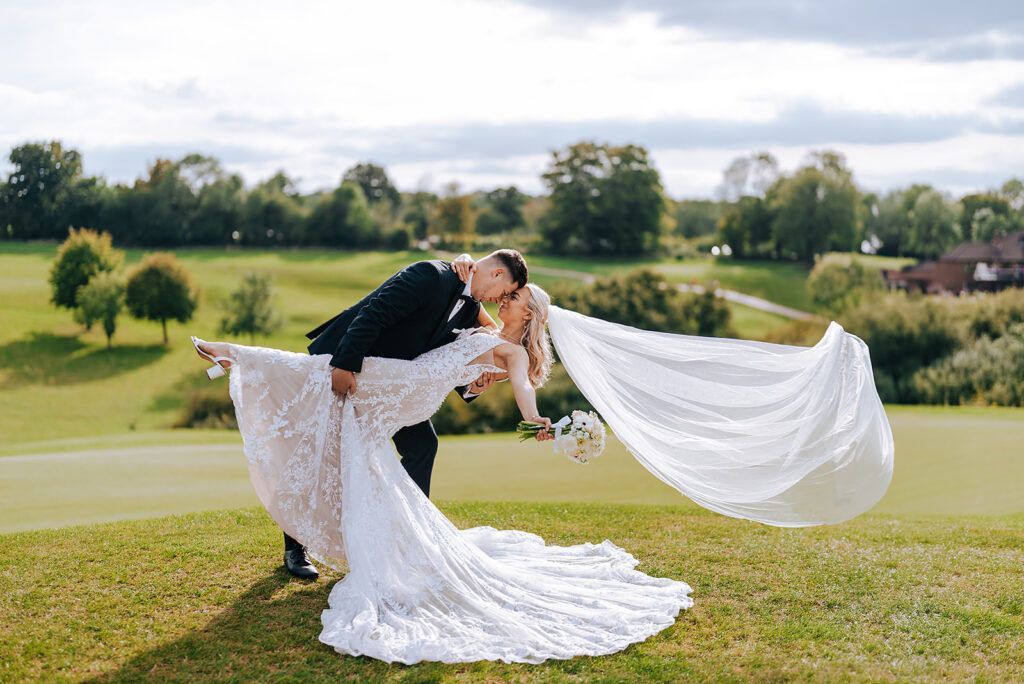 Groom dipping bride in countryside setting with flowing veil, candid wedding photography in Sussex by Alex Buckland Photography